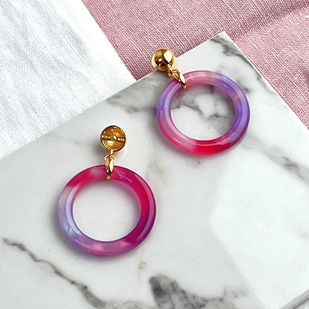 Tortoiseshell hoop earrings in purple from the Audrey collection by Misia Mae. The earrings are presented on a white marble top and white and pink linen cloth