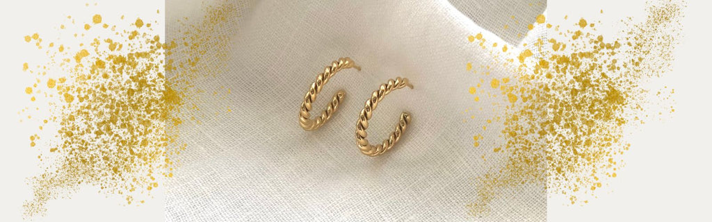 twisted gold earrings on a white linen background with gold sparkle