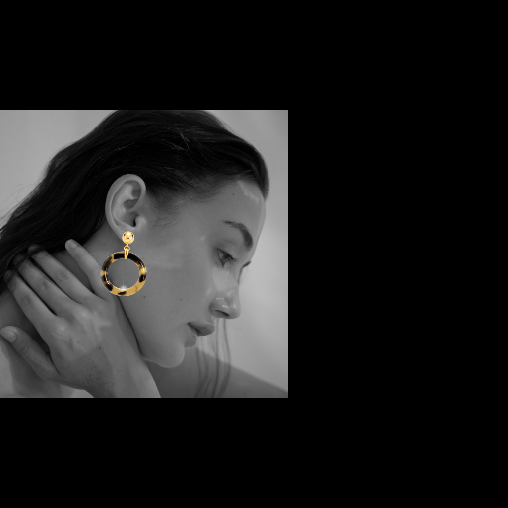 Close-up of a person wearing gold hoop earrings with a black and white background