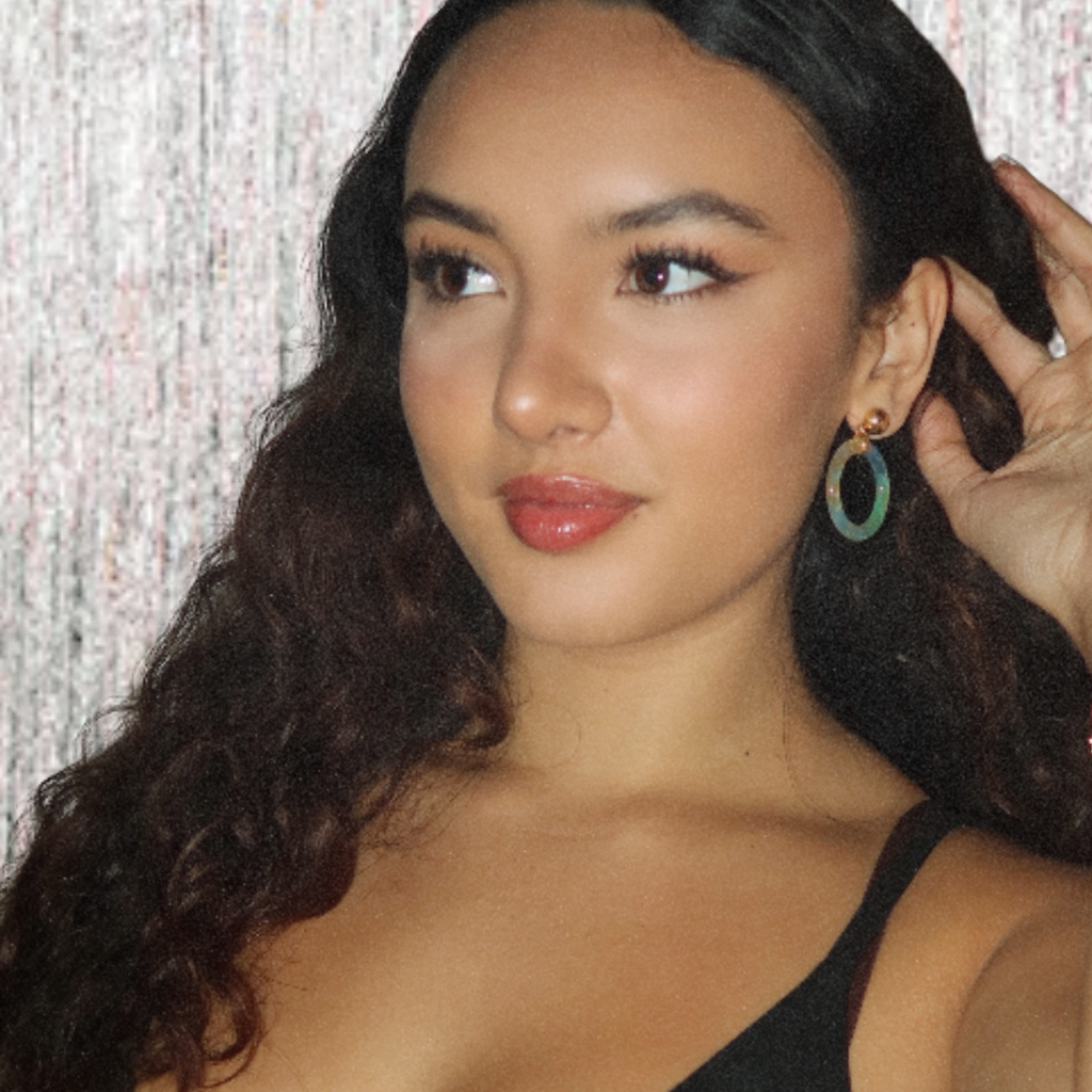 Woman with long dark hair and blue earrings against a textured white and silver background
