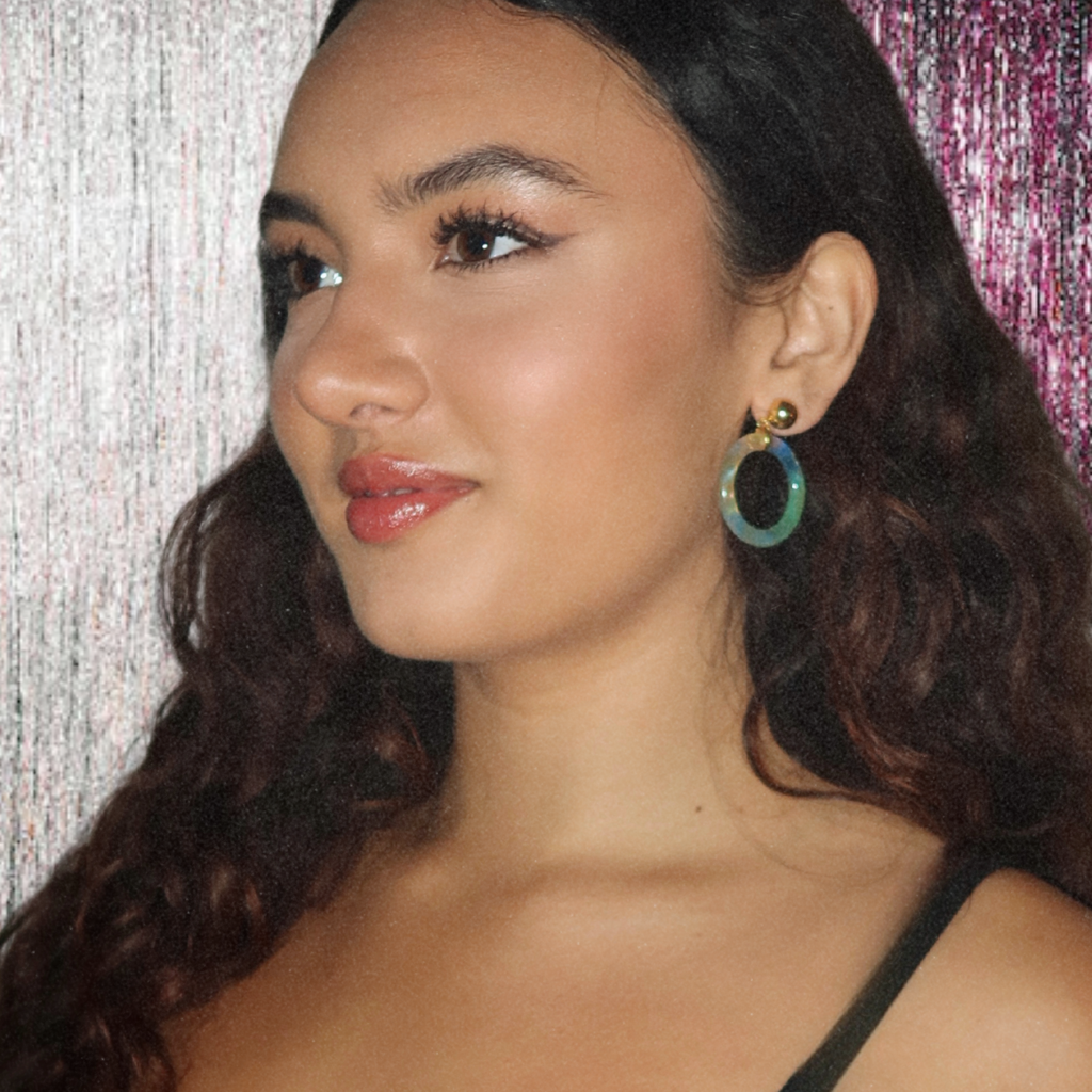 Woman wearing blue tortoiseshell hoop earrings with a textured background