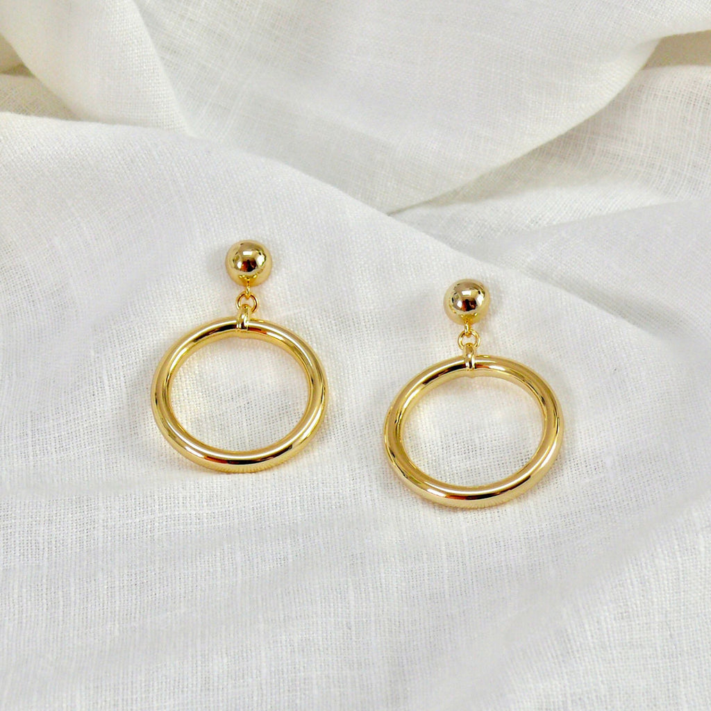 chunky gold earrings on a white linen cloth. The earrings are by Misia Mae