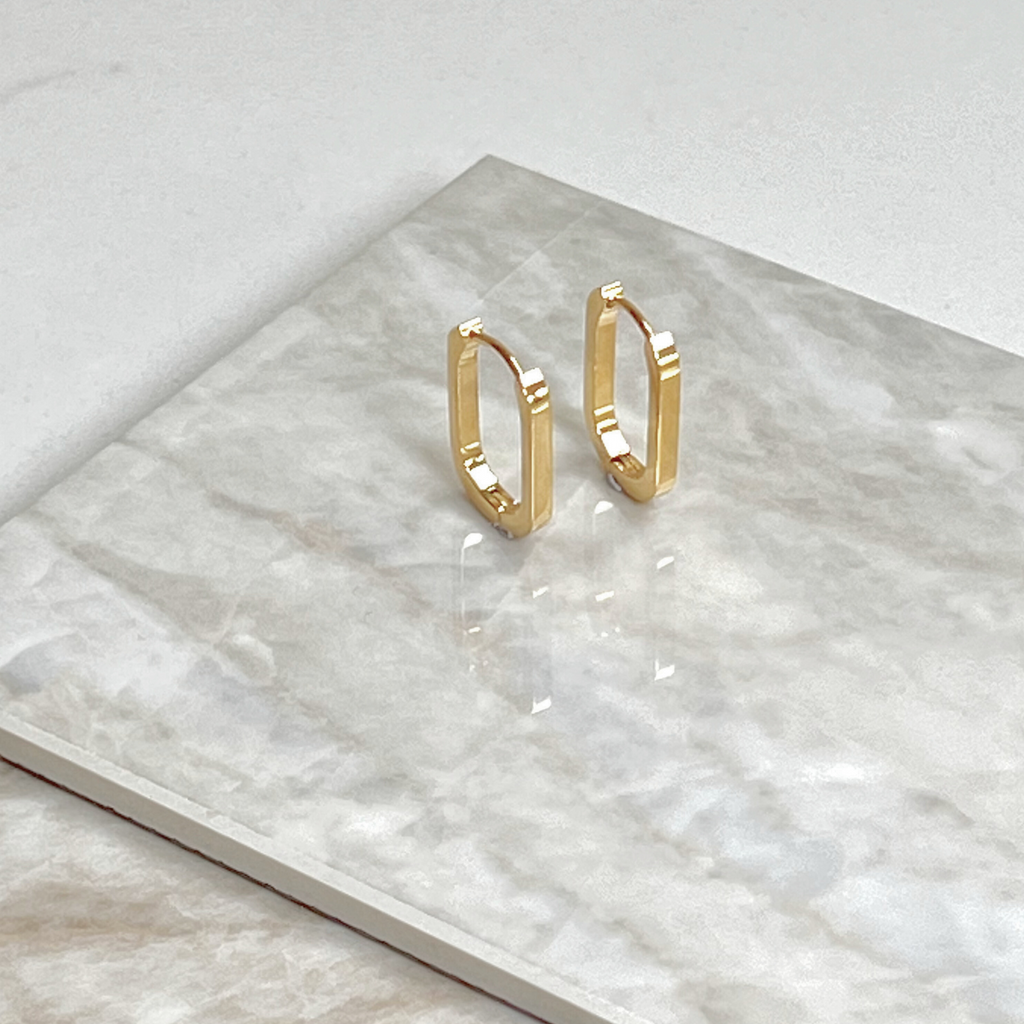 Gold oval earrings by Misia Mae on a marble top