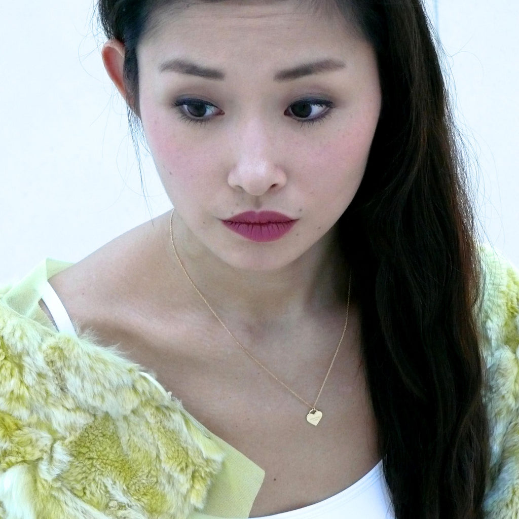 A brunette woman wearing heart gold necklace by Misia Mae