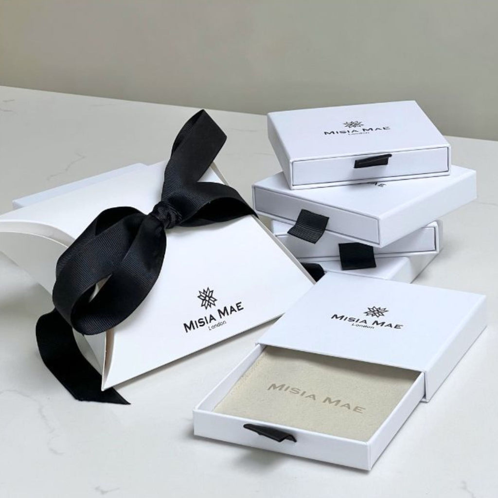 White jewelry boxes with black ribbons and 'Misia Mae' branding on a light gray background