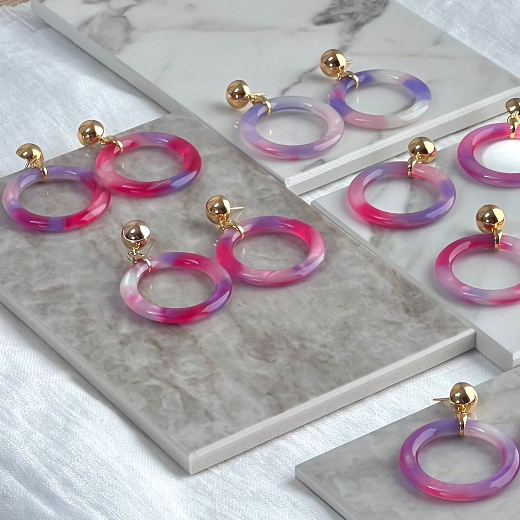 A selection of tortoiseshell hoop earrings in purple from the Audrey collection by Misia Mae. The earrings are presented on a white marble top and white  linen cloth