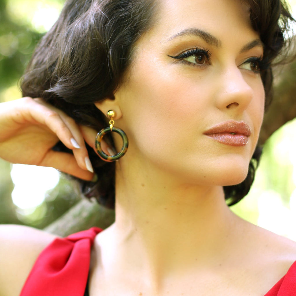 A brunette model in a red dress wearing animal print earrings from the Audrey collection by Misia Mae