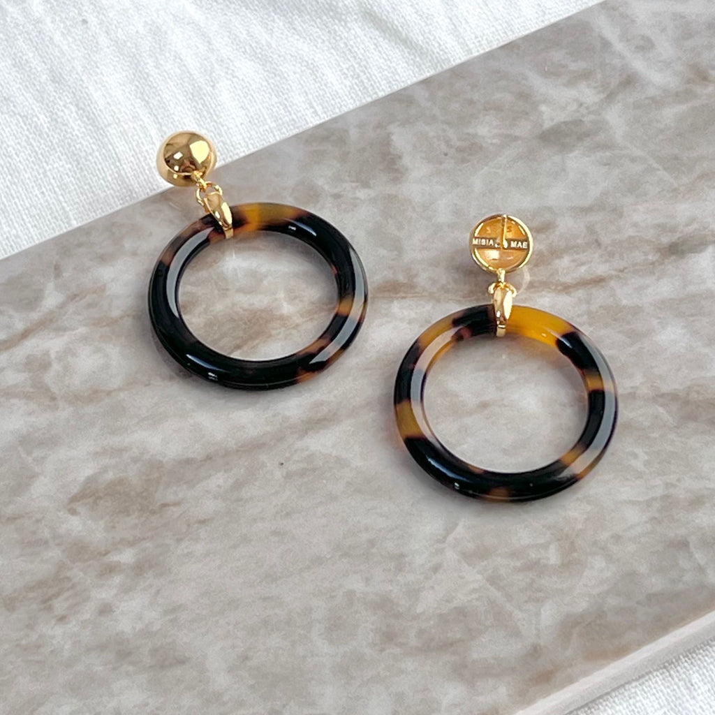 animal print earrings from the Audrey collection by Misia Mae. The tortoiseshell hoop earrings are placed on a marble decton top and a white linen cloth. 
