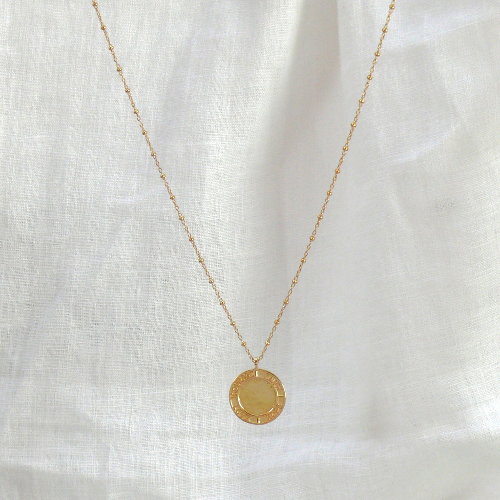 Gold pendant necklace on a white linen background. The necklace is by Misia Mae 
