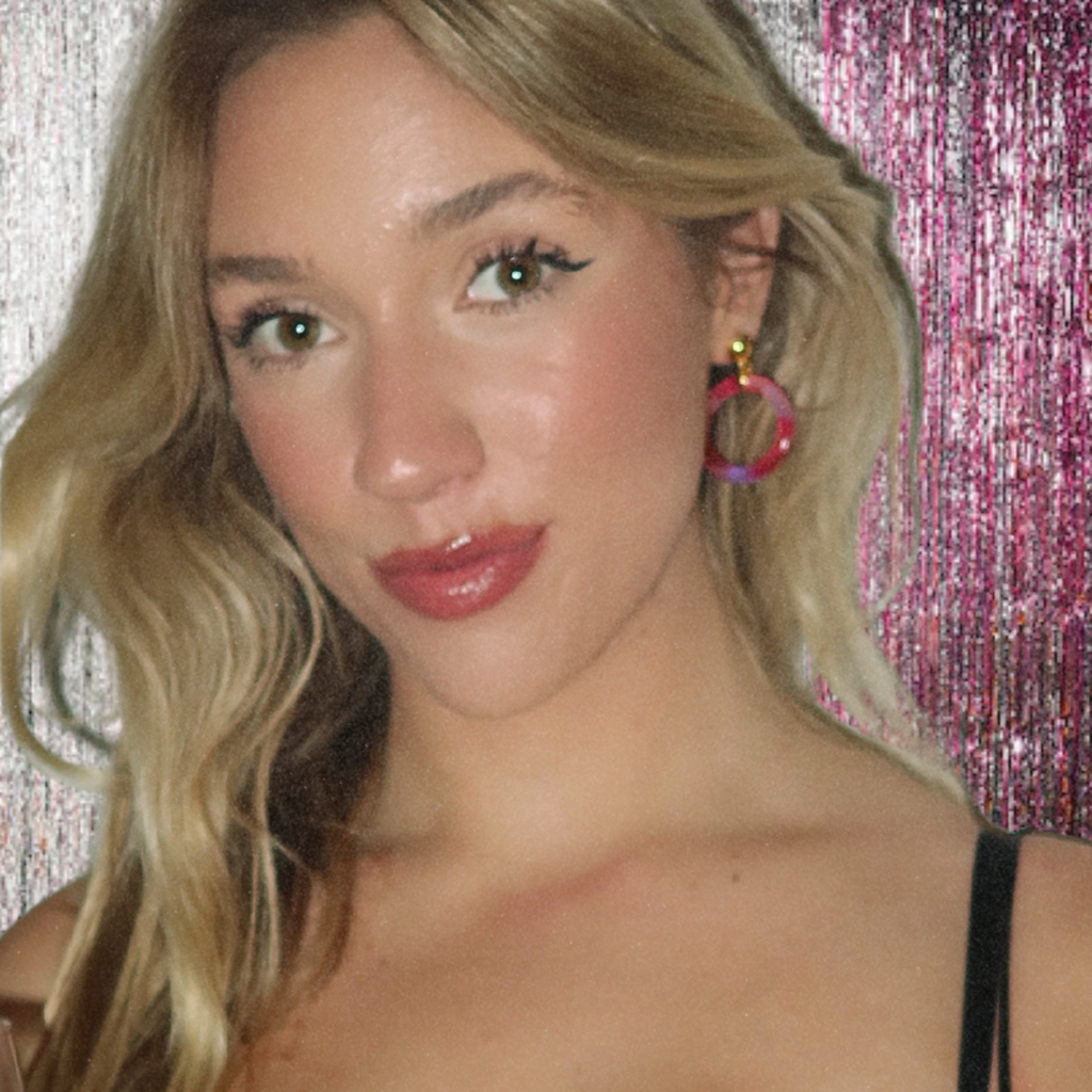 Woman with blonde hair and pink tortoiseshell hoop earrings against a glittery pink background