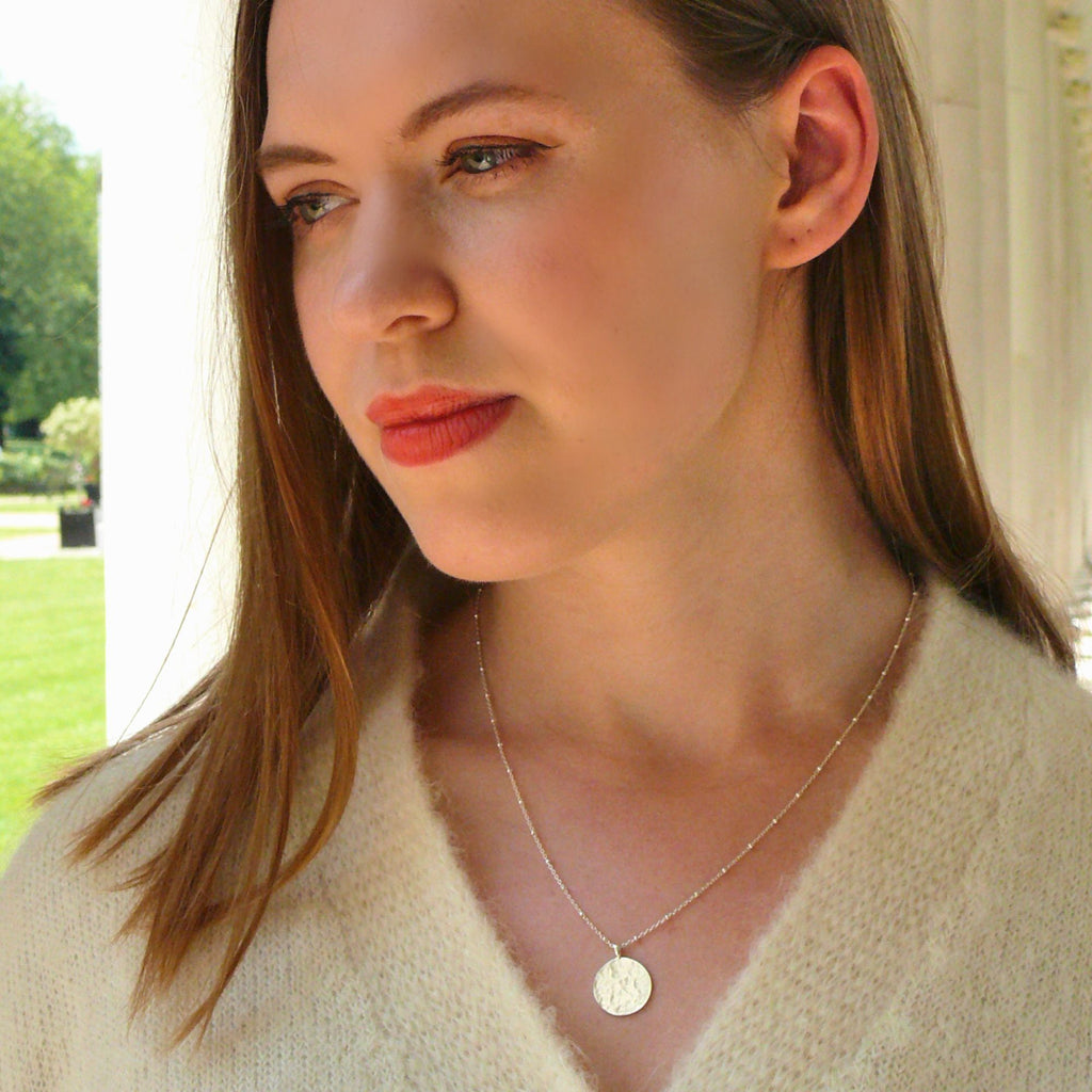 A blonde woman wearing a silver pendant necklace from the Thea collection by Misia Mae