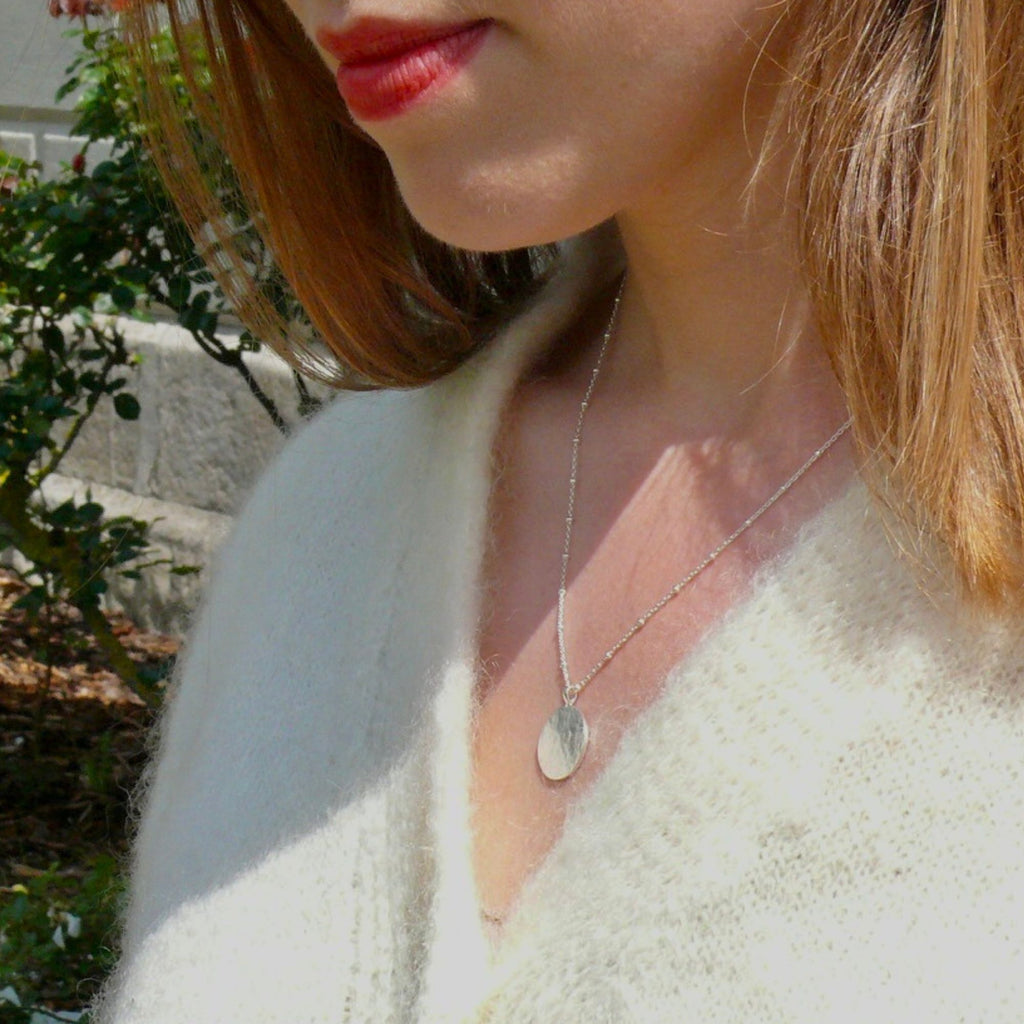 A blonde woman wearing a cream knitted top  silver pendant necklace from the Thea collection by Misia Mae