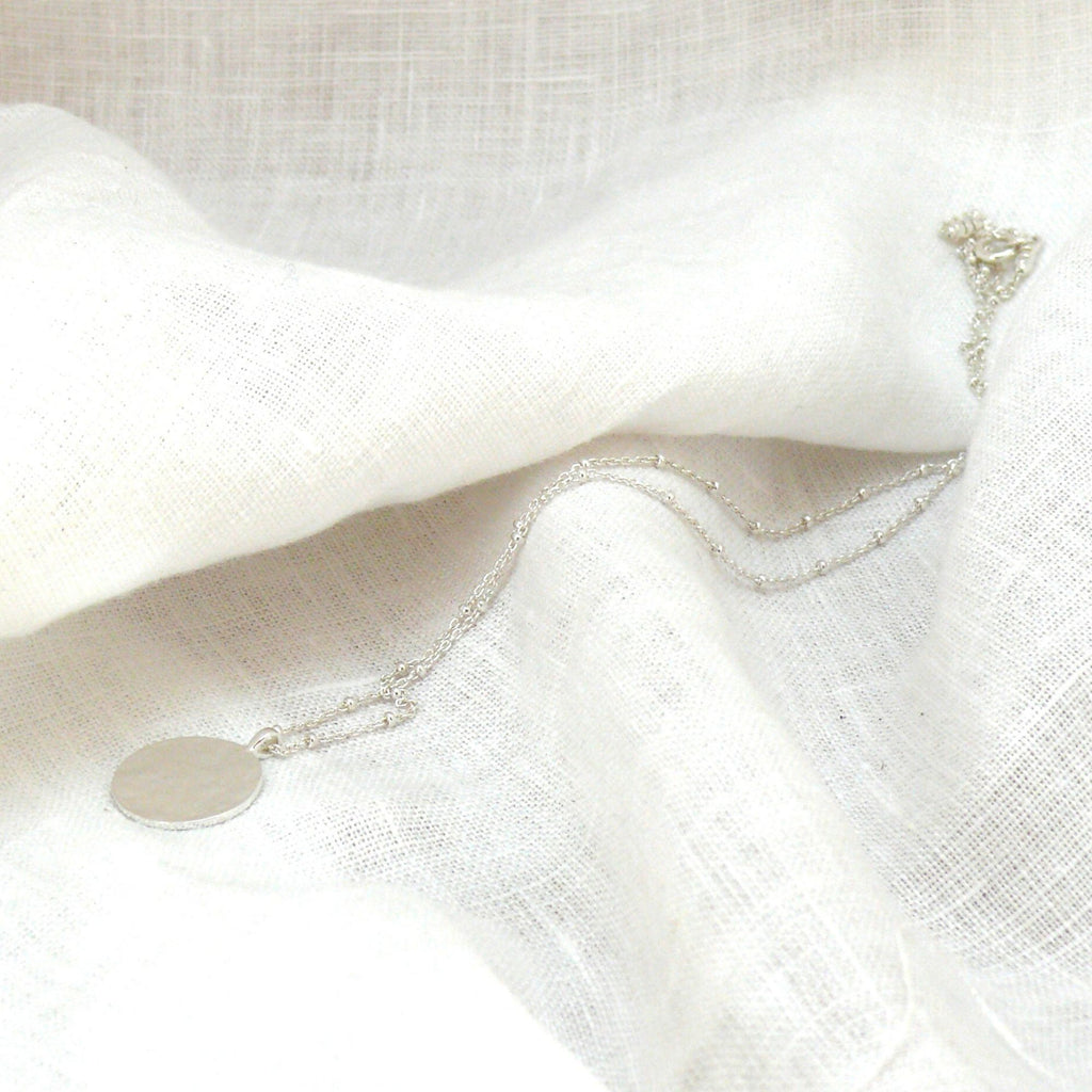 silver pendant necklace on a white linen fabric by Misia Mae