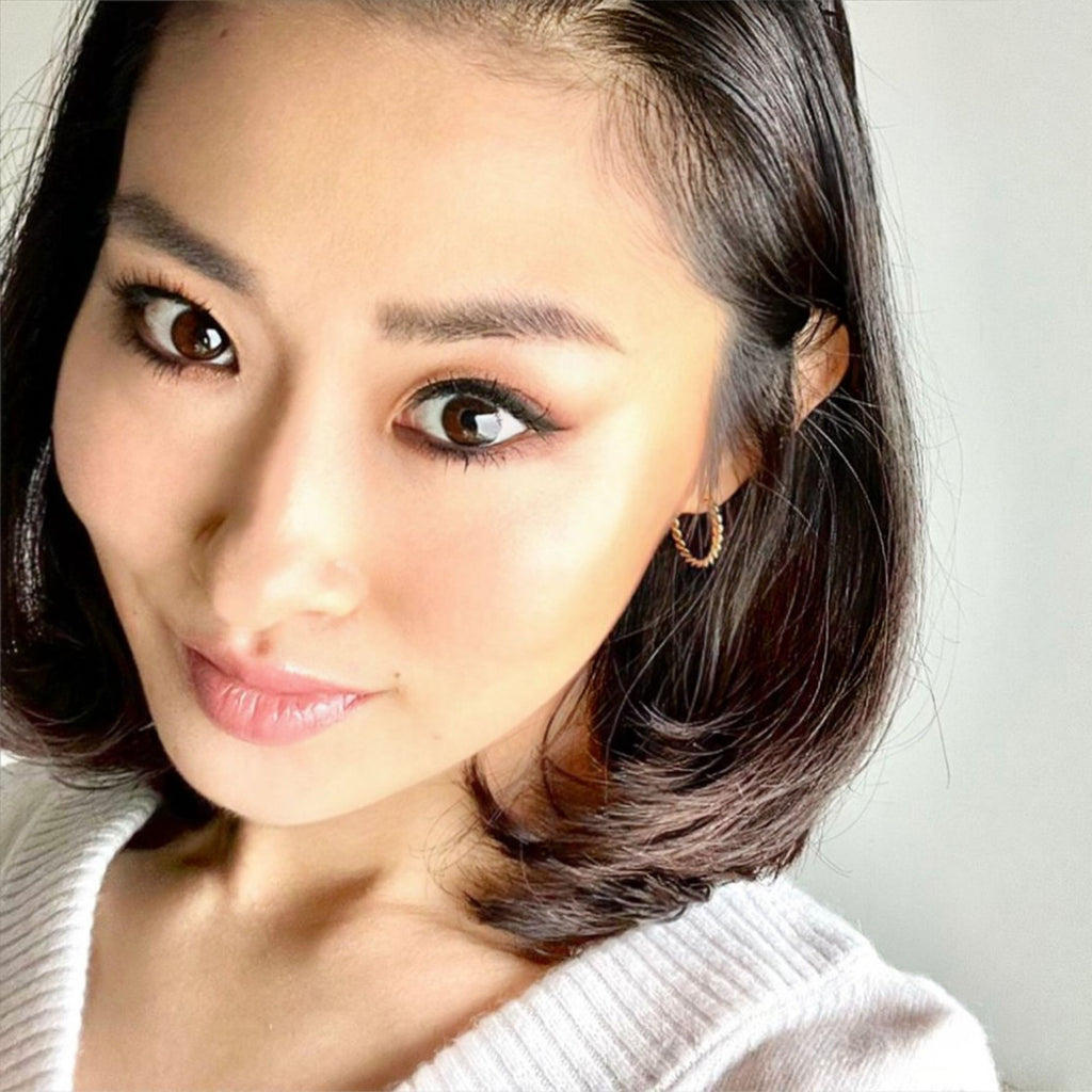 a dark haired woman wearing a beige top and twisted gold earrings by Misia Mae